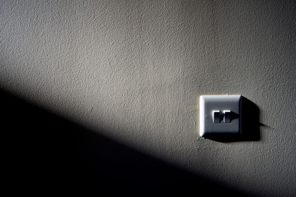 A light switch on a textured wall with contrasting shadow and light, creating a minimalist aesthetic.