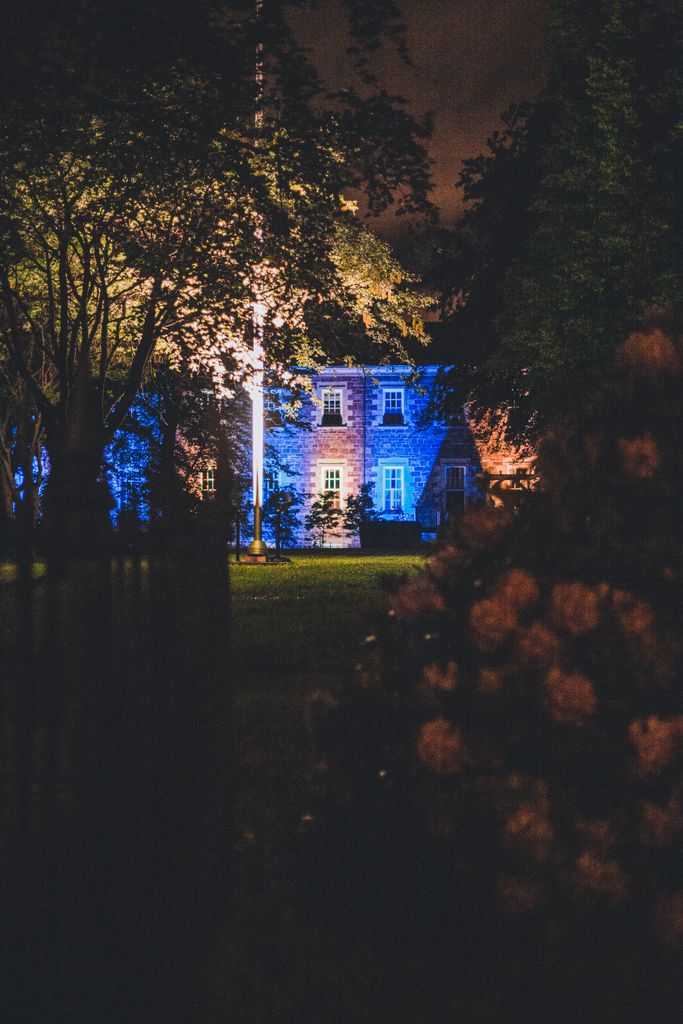 A beautifully illuminated house at night, surrounded by trees and garden flowers.